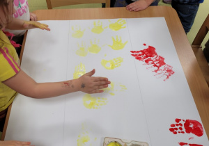 Dzieci odbijają pomalowane farbą rączki na kartonie