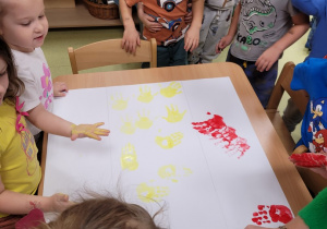 Dzieci odbijają pomalowane farbą rączki na kartonie