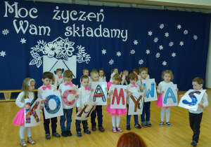 Dzieci recytują wiersze trzymają kartki z literkami tworząc napis kochamy was