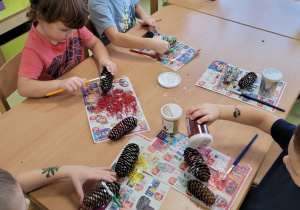 Dzieci posypują pomalowane szyszki brokatem