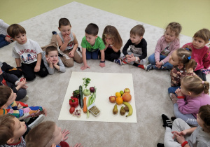 Dzieci siedzą w kole, na środku leżą warzywa i owoce