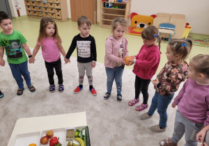Dzieci stoją w kole podając sobie owoc