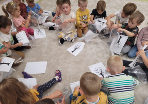 Dzieci wkładają kartki z ilustracją drzewa do koszulek foliowych