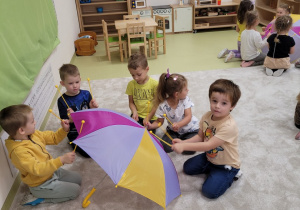 Dzieci naśladują krople deszczu uderzając pałeczkami o parasol