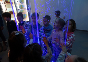 Dzieci oglądają bombelki na podświetlonym na niebiesko panelu.