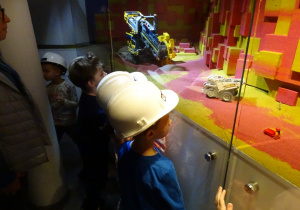 Dzieci w kaskach oglądają makietę pojazdów górniczych.
