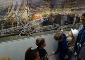 Dzieci w kaskach oglądają makietę pojazdów górniczych.