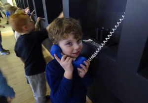 Chłopiec trzyma niebieską słuchawkę telefoniczną w ręku.