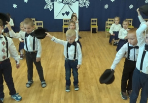 Dzieci tańczą - dziewczynki z goździkami, chłopcy z kapeluszami.