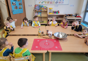 Dzieci w fartuszkach siedzą przy stole na którym czekają składniki