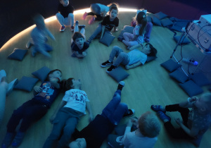 Dzieci leżą na poduszkach oglądają film wyświetlany w kopule