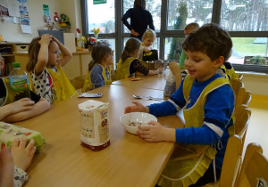 Dzieci siedzą przy stole i obserwują robienie ciasta.