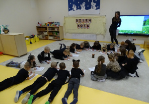 Dzieci leżą na podłodze i piszą coś na kartkach.