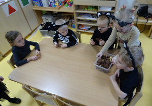 Dzieci siedzą przy stoliku i częstują się ciasteczkami.