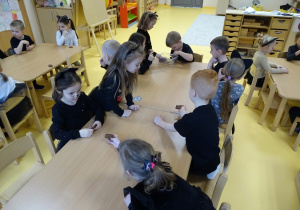 Dzieci siedzą przy stoliku i częstują się ciasteczkami.