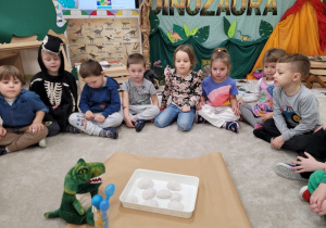 Dzieci siedzą wokół pojemnika z jajkami dinozaurów