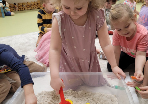 Dzieci poszukują w piasku kinetycznym figurek dinozaura