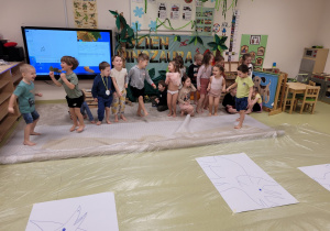 Dzieci boso czekają na malowanie stopami sylwet dinozaurów