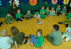 Dzieci ubrane na zielono siedzą w kole z paniami