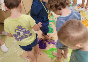 Dzieci malują stopami sylwety dinozaurów