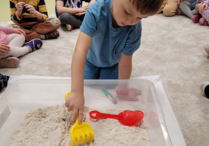 Kacperek szuka w piasku figurek dinozaurów