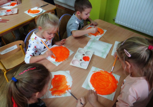 Dzieci malują papierowe talerzyki na pomarańczowo
