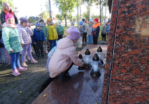 Dzieci stawiają znicz pod pomnikiem niepodległości