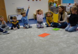 pani siedzi z dziećmi na dywanie i pokazuje kartki