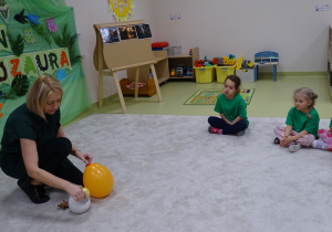 03 Pani trzyma w rękach balon. Dzieci uczą się, że05 Pani rozkłada ślady dinozaurów i tłumaczy na czym będzie polegała zabawa dinozaury rodziły się z jajek
