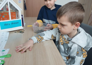 Chłopiec przelicza grosze, drugi trzyma pojemnik z pieniędzmi