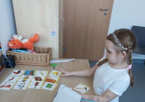 Dziewczynka układa po 3 obrazki wysłuchanych dźwięków