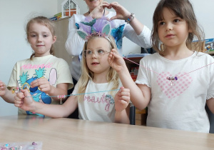 Dziewczynki prezentują zrobioną biżuterię z panią logopedą