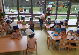 Dzieci w czapkach kucharskich siedzą przy stoliczkach.