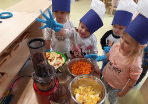 Dzieci wkładają owoce i warzywa do wyciskarki.