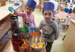 Dzieci wkładają warzywa i owoce do wyciskarki.