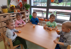 Dzieci siedzą przy stoliku i piją sok.