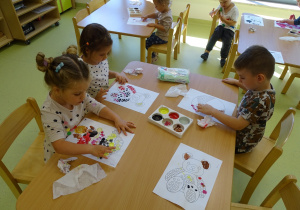 Dzieci wykonują przy stoliku pracę plastyczną z wykorzystaniem farb.