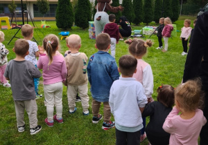 Dzieci biorą udział w zabawach ruchowych z animatorką na trawie.