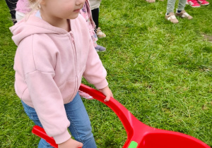 Dziecko prowadzi taczkę z piłeczką.