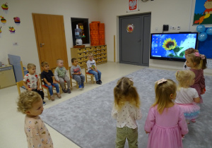 chłopcy siedzą na krzesełkach a dziewczynki stoją