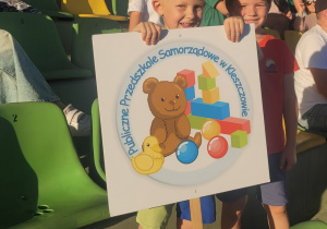 Kubuś z Wojtusiem na trybunach boiska z logo przedszkola