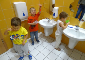 dzieci stoją przy umywalce i myją zęby