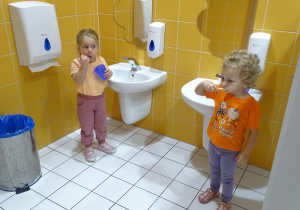dzieci stoją przy umywalce i myją zęby