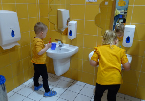 dzieci stoją przy umywalce i myją zęby