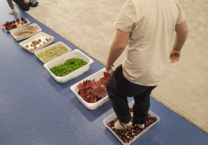 Dzieci idą bez butów po ścieżce sensorycznej ułożonej z darów jesieni