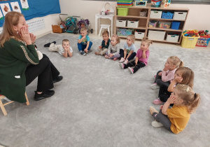 Logopeda dotyka dłonią prawego policzka, dzieci naśladuja