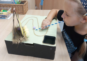 Dziewczynka wykonuje ćwiczenie oddechowe ze słomką na torze z jajkiem