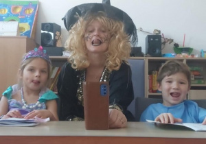 Dziewczynka, logopeda w stroju czarownicy i chłopiec oblizują językiem usta