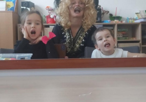 Dziewczynka, logopeda w stroju czarownicy i chłopiec kląskają językiem