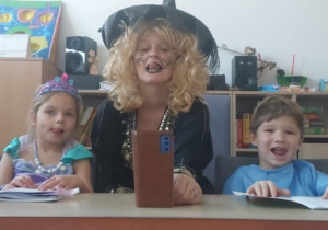 Dziewczynka, logopeda w przebraniu i chłopiec oblizują górną wargę